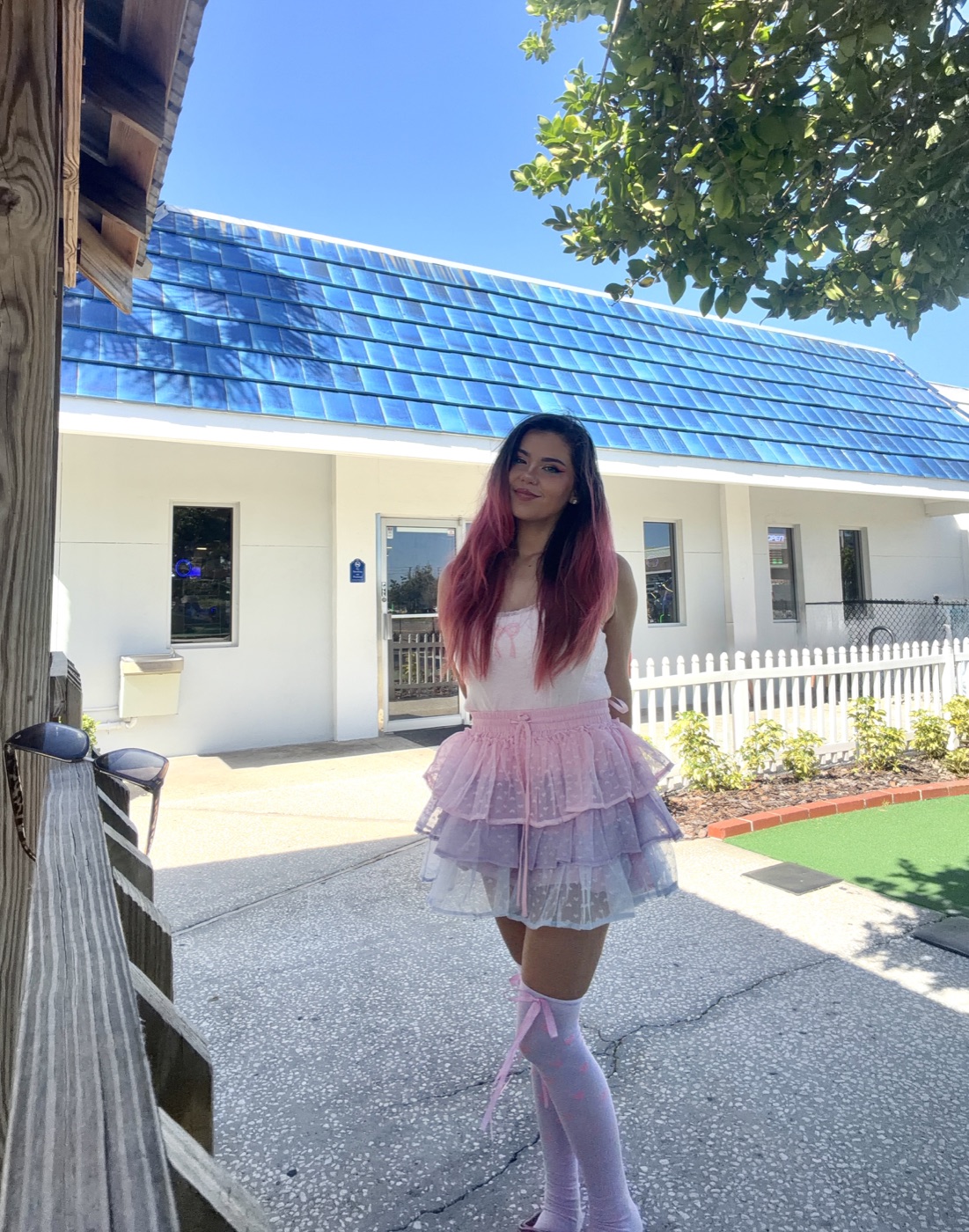 Kate with pink hair, wearing a pink and lilac outfit outdoors.